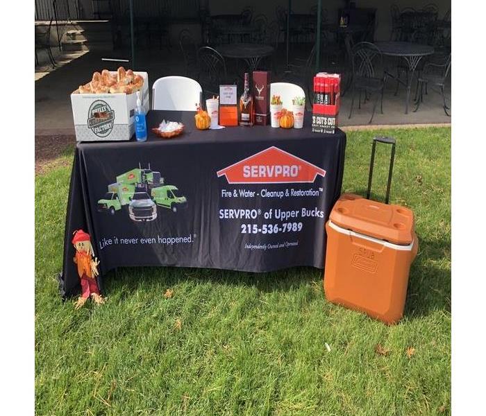 A SERVPRO table sits on a golf green with soft pretzels and other giveaways. An orange cooler sits on the right
